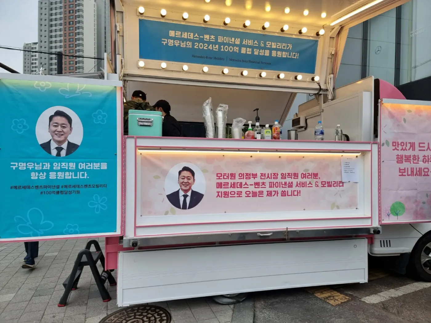 구명우 딜러의 얼굴이 실린 배너가 걸린 커피차 행사 현장